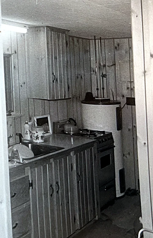 The original kitchen: the dark-green stove, and the old water heater that gave us fits — the shared well would lose water, the heating eleme…